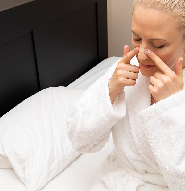 Frau im weißen Bademantel klebt sich Pflaster auf die Nase