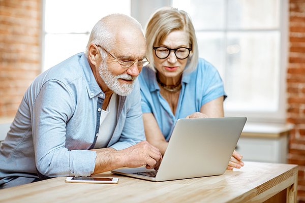 Älteres Paar sitzt vor Laptop und schaut auf Bildschirm