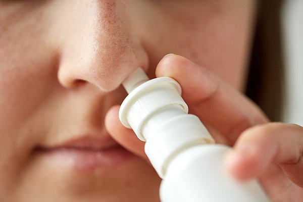 Großaufnahme einer Frau, die sich Nasenspray in die Nase sprüht