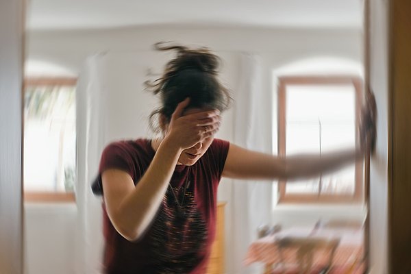 Verwackeltes Foto: Jüngere Frau stützt sich an Türrahmen ab und hat Hand an Stirn weil schwindelig
