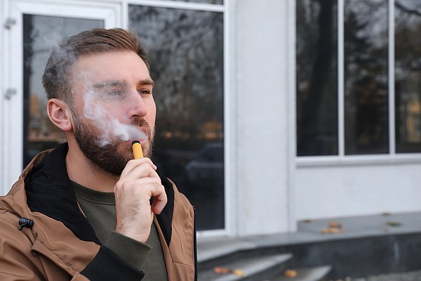 Junger Mann mit E-Zigarette steht draußen